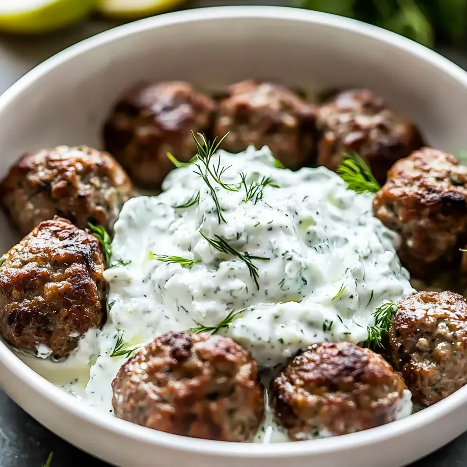 A serving of meatballs topped with creamy cucumber sauce.