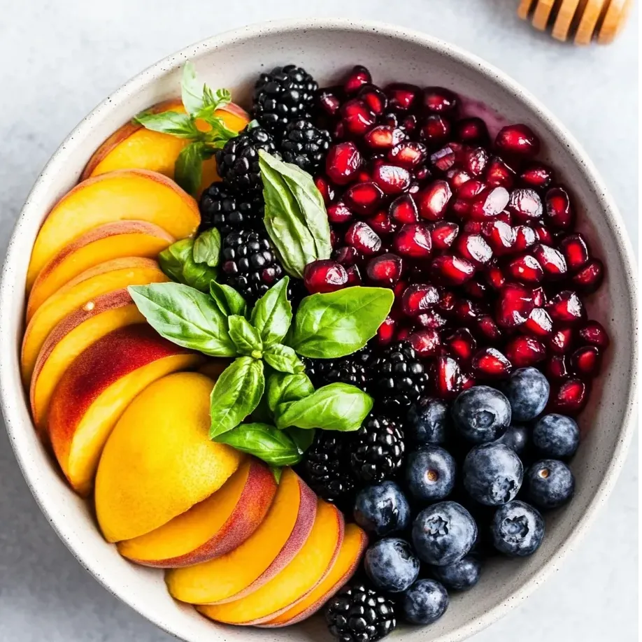 Blueberries, blackberries, peach slices, and a drizzle of honey in a bowl.
