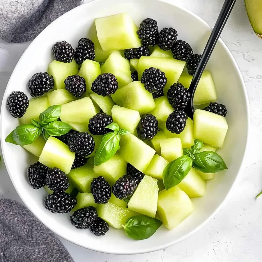 A bowl featuring melon chunks, blackberries, and basil leaves beautifully arranged.