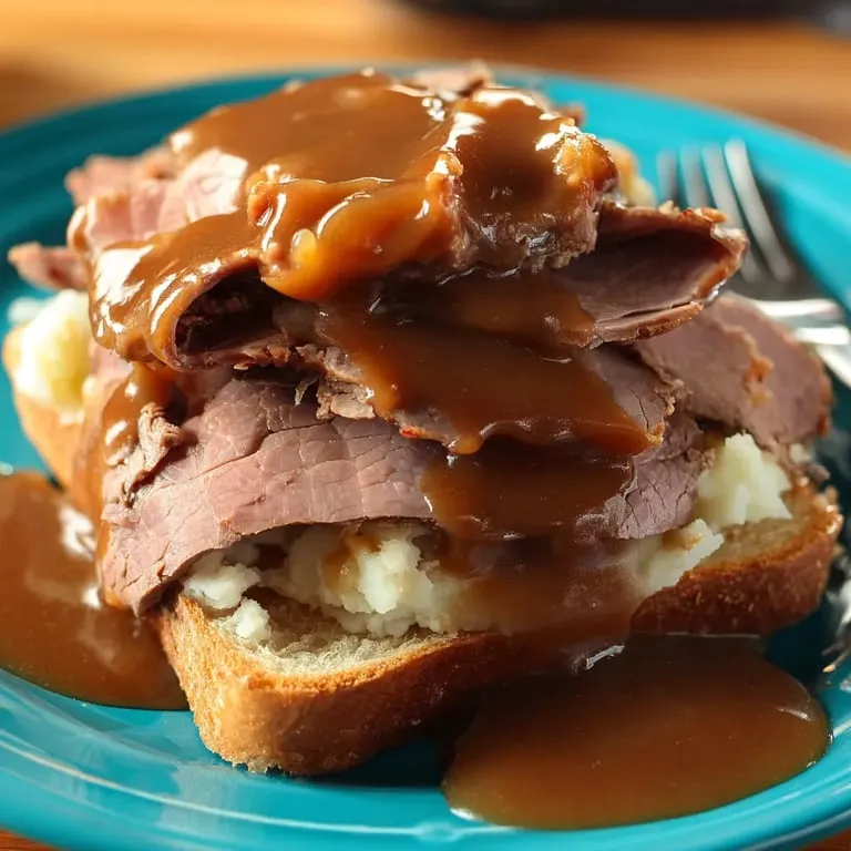 Slices of meat and mashed potatoes on bread under gravy.