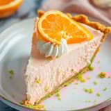 A colorful slice of creamy orange pie with a bright orange garnish on top.