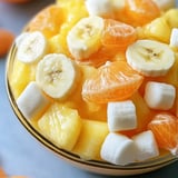 A fruit bowl featuring bananas, oranges, and fluffy marshmallows.