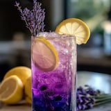 A cool purple drink in a glass with lemon slices and lavender sprigs.