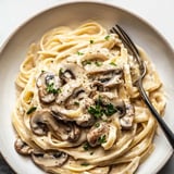 Bowl filled with pasta and mushrooms plus fresh herbs.