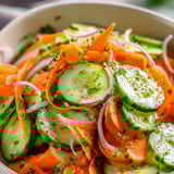 Chopped cucumbers, carrots, and onions in a serving bowl.